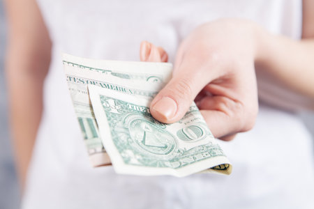 young woman gives money on gray backgroundの写真素材