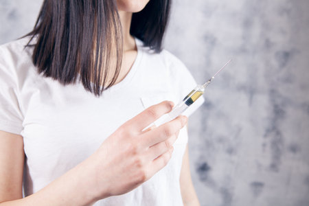 young woman holding a syringe in her hands on a gray backgroundの写真素材