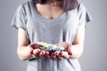 young girl holding pills in hand on gray backgroundの写真素材