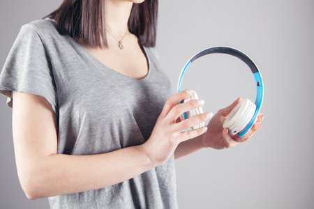 young woman holding big headphones on gray backgroundの写真素材