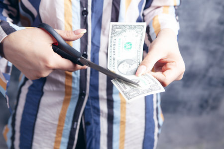 young woman cuts dollar with scissorsの写真素材
