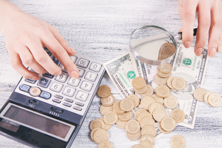woman counts money with calculator and looks with magnifying glassの写真素材