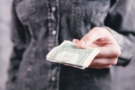young woman gives money on gray background