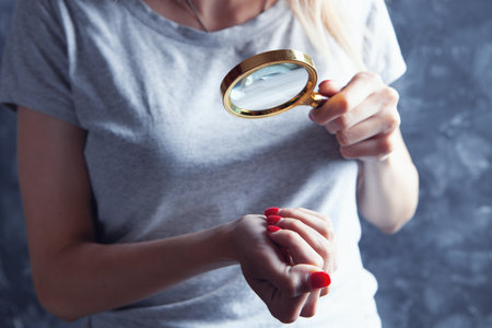 young girl looks at painted nails with a magnifying glassの写真素材