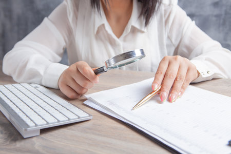 woman looking at paper with a magnifying glass in front of a computer
