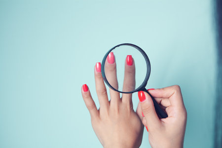 young girl looks at painted nails with a magnifying glassの写真素材