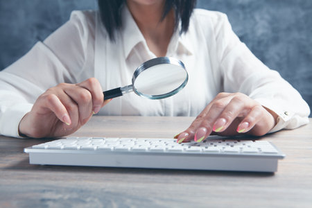 woman looking at the keyboard with a magnifying glassの写真素材