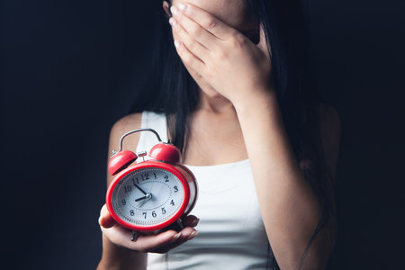 woman holding an alarm clock in her hand and covering her face
