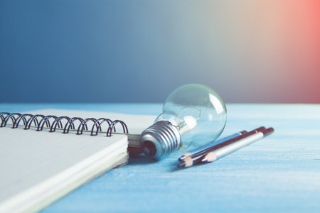 on the table a notebook, pens and a light bulbの写真素材