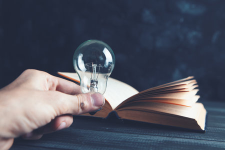 hand holds a light bulb next to a book
