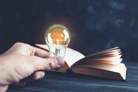 hand holds a light bulb next to a bookの写真素材