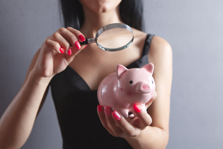 woman examines a piggy bank with a magnifying glassの写真素材