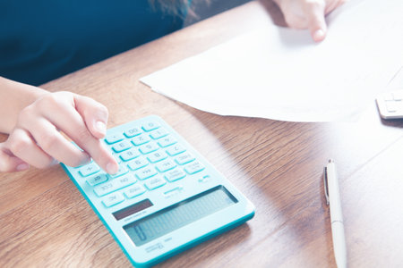 young woman counts on calculator and makes notes on papersの写真素材
