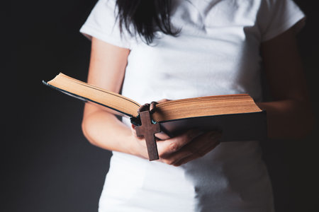 woman praying on book holding cross