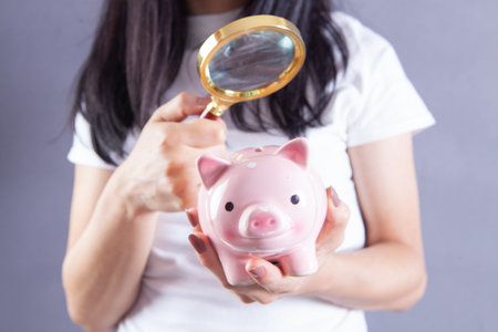 woman examines a piggy bank with a magnifying glassの写真素材