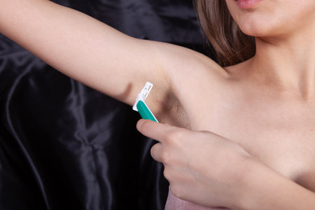 woman in bathrobe shaving her armpit with a razorの写真素材