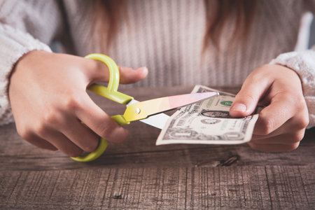 young woman cuts money with scissorsの写真素材
