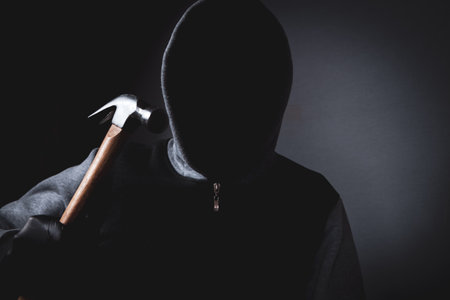 man with a hood and a mask on his face threatens with a hammerの写真素材