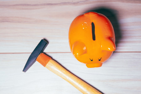 orange piggy bank on wooden table with hammer
