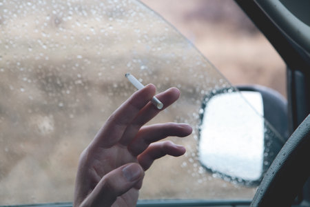 hand holding a cigarette in front of a windowの写真素材