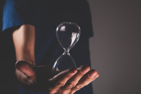 a male hand holds a hourglass on a dark background. time to work.