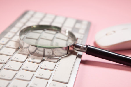 Keyboard and magnifying glass on pink background. Business concept.