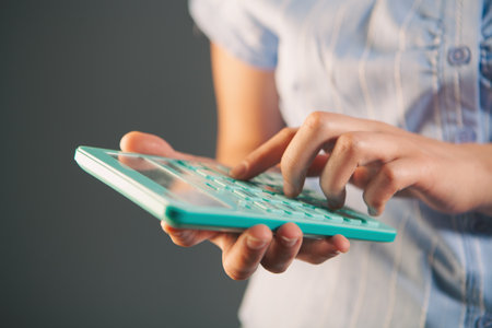 Close-up image of a woman using a calculator on gray backgroundの写真素材