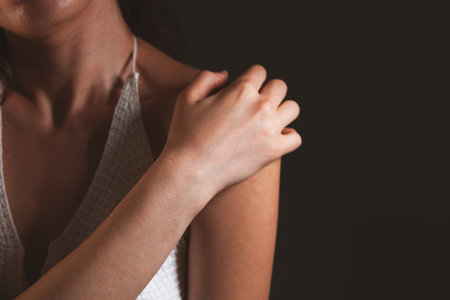 Close-up of woman suffering from pain in shoulder against black backgroundの写真素材