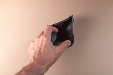 Man's hand holding empty wallet on beige background, closeup