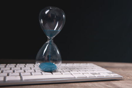 Hourglass and computer keyboard on wooden table. Time management concept.