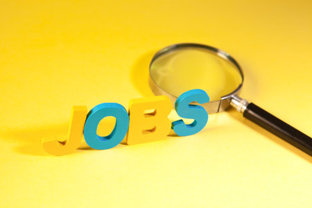 Wooden letters forming the word Jobs and magnifying glass on yellow backgroundの写真素材