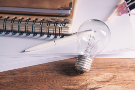 Light bulb with notebook and pencil on wood table background, idea conceptの写真素材