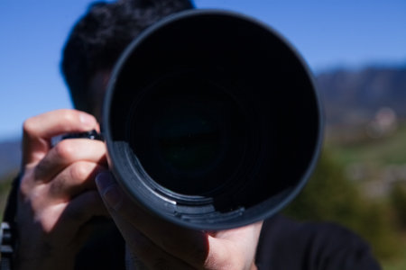 Photographer taking photo with professional camera in mountains. Focus on lens.の写真素材