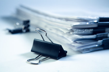 Close up of pile of business papers and binder clip on white background