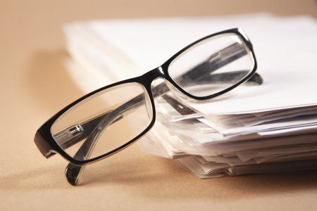 Close up of eyeglasses with stack of papers on brown backgroundの写真素材