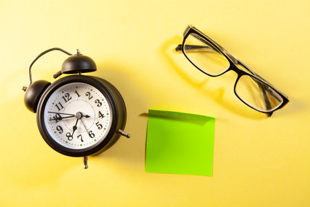 Alarm clock, eyeglasses and sticky note on yellow backgroundの写真素材