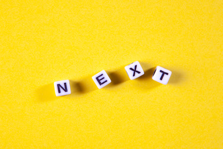 The word Next spelled with toy cubes on a yellow background. Top view.の写真素材