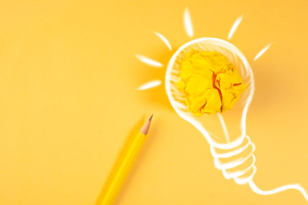Light bulb and crumpled paper ball with pencil on yellow backgroundの写真素材