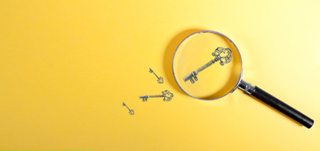 Key and magnifying glass on a yellow background. The concept of finding a solution.