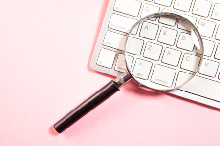 Magnifying glass and computer keyboard on a pink background. Top viewの写真素材