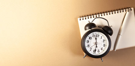 Alarm clock and notebook on brown background. Time management concept.