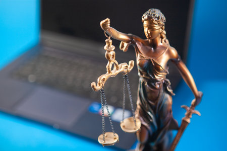 Lady Justice statue and laptop on blue background. Law and justice concept.