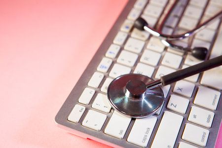 Stethoscope on a laptop keyboard on a pink background with copy spaceの写真素材