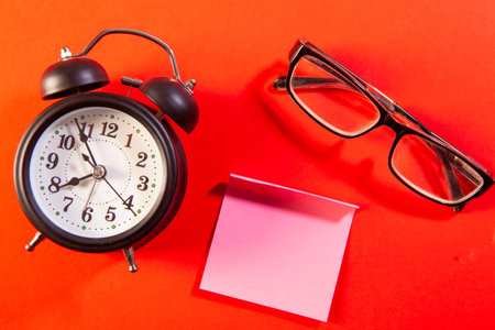 Retro alarm clock, eyeglasses and sticky note on red backgroundの写真素材
