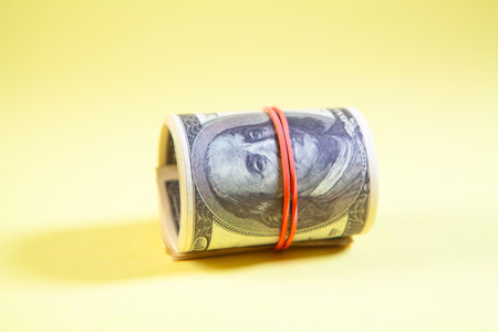 A roll of one hundred dollar banknotes on a yellow background.の写真素材