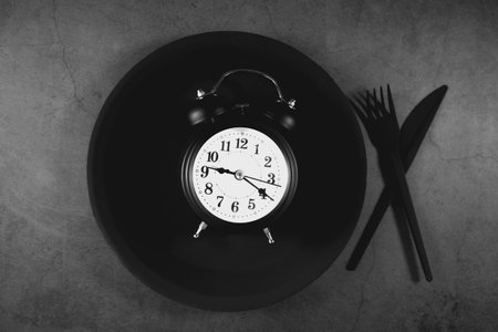 Alarm clock on black plate with cutlery on gray backgroundの写真素材