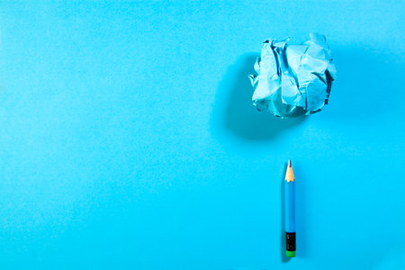 Blue crumpled paper ball and pencil on blue background with copy spaceの写真素材