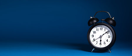 Black alarm clock on blue background with copy space. Time concept.