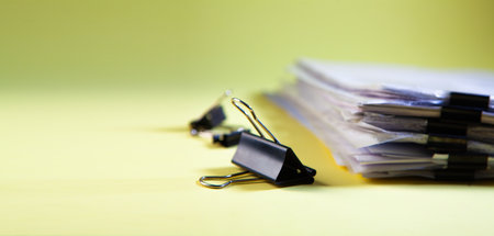 Close up of a pile of papers and binder clips on a yellow background