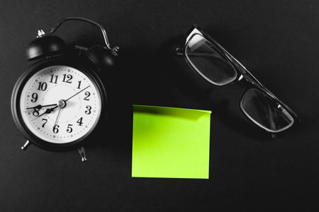 Retro alarm clock, eyeglasses and green sticky note on black backgroundの写真素材